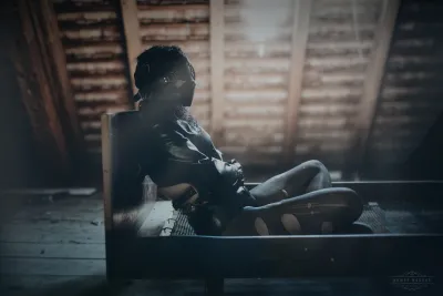 Person in bondage gear sitting in an abandoned attic with light filtering through the roof