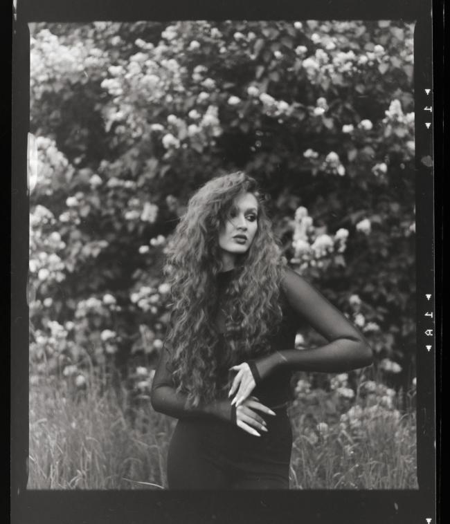 Black and white portrait of a model with curly hair in a natural setting.