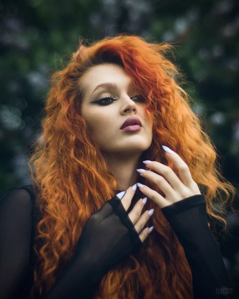 Kobieta z długimi kręconymi rudymi włosami i czarną siateczkową bluzką