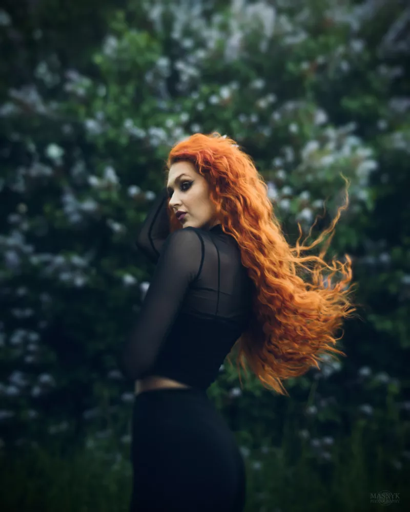 Kobieta z długimi kręconymi rudymi włosami i czarną siateczkową bluzką