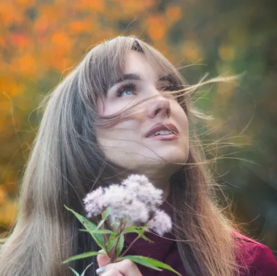 Porträt einer Frau mit einer Blume vor herbstlichen Blättern