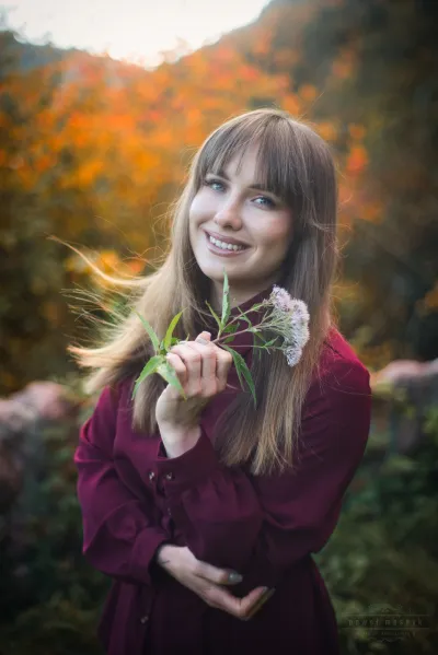 Portret uśmiechniętej kobiety trzymającej kwiaty na tle jesiennego krajobrazu w Neckarsteinach