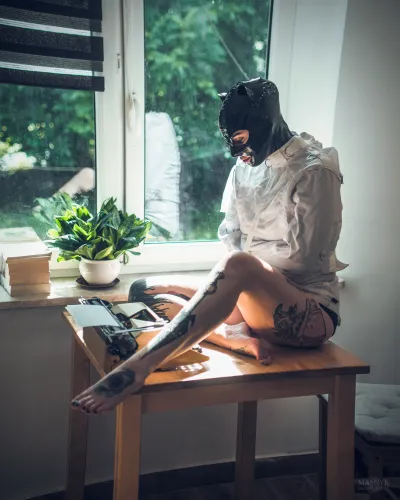 Girl in a latex mask sitting on a table by the window