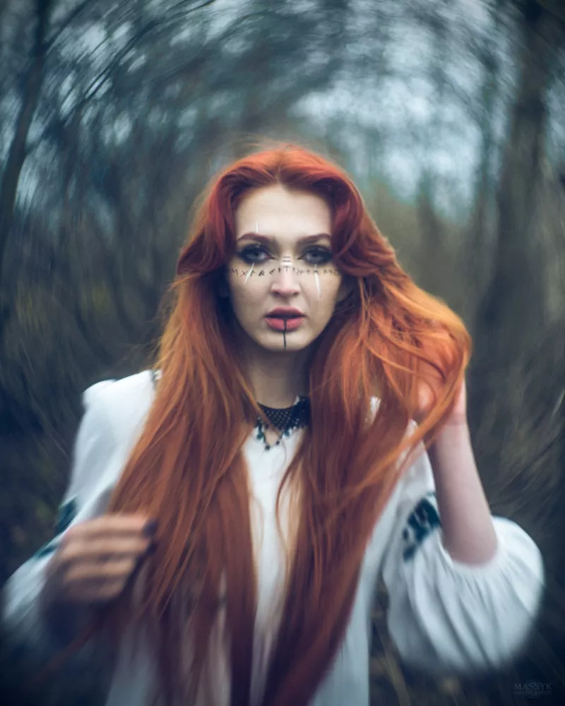 Portrait of a woman in a forest with long red hair and face markings