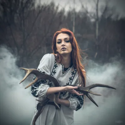 Artistic portrait of a woman with antlers in a misty forest setting