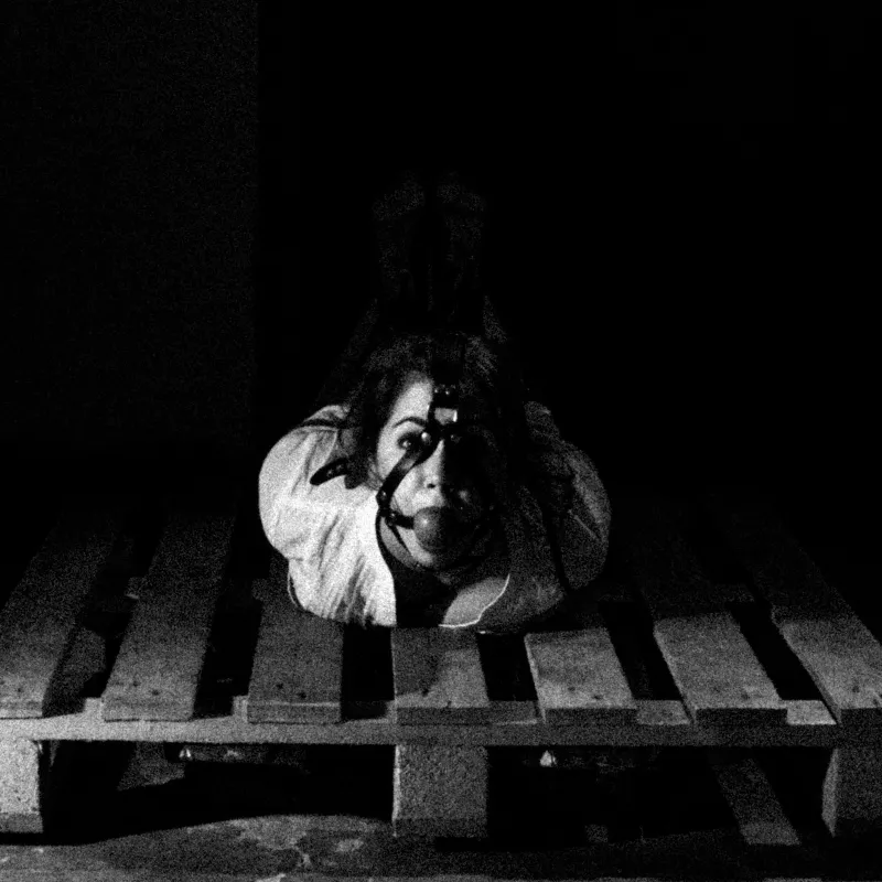 Model in a stylized BDSM session, wearing a ball gag and tied in a hogtie position