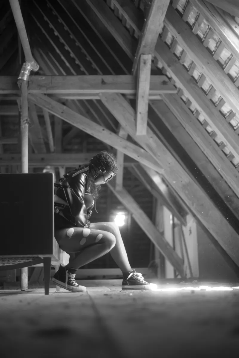 Person in a leather jacket sitting in an abandoned attic with beams of light.