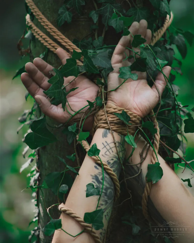 Tattooed hands tied with rope around a tree with ivy