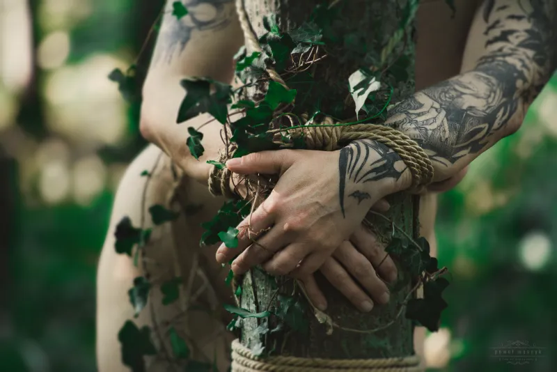Tattooed hands tied with rope around a tree with ivy