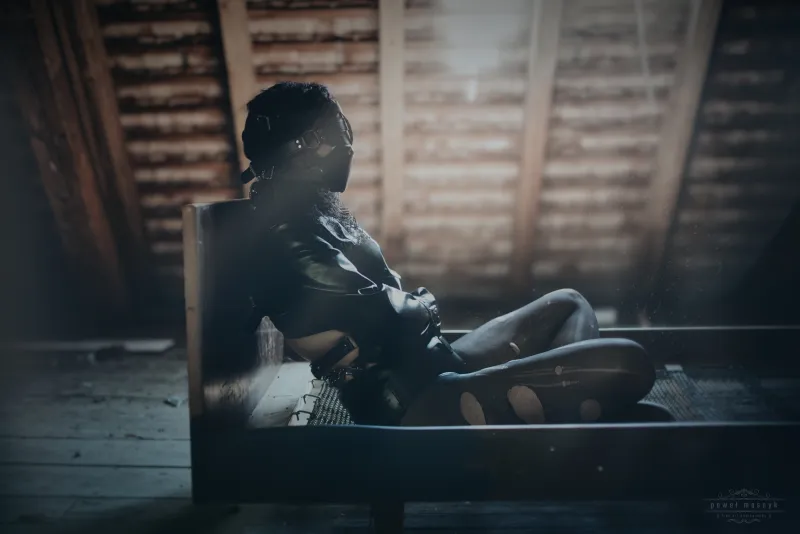 Person in bondage gear sitting in an abandoned attic with light filtering through the roof