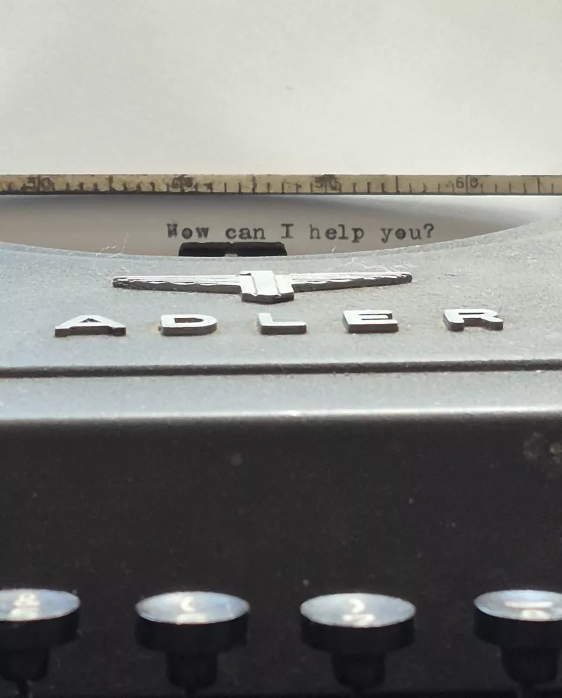 Nahaufnahme einer Vintage-Schreibmaschine mit dem Text 'How can I help you?' darauf.