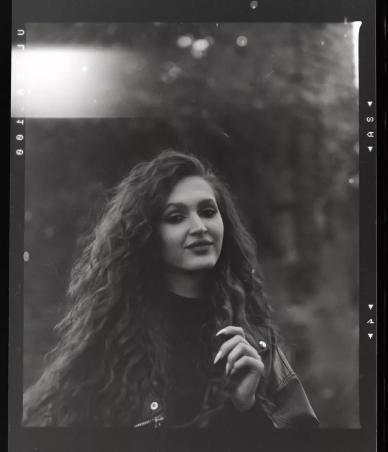 Schwarz-Weiß-Porträt einer Frau mit lockigem Haar in einer ruhigen Outdoor-Umgebung