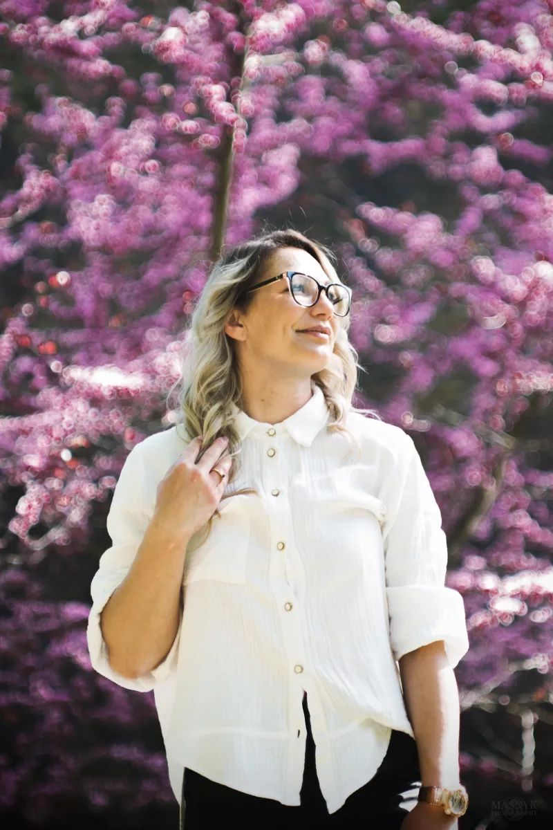 Kobieta uśmiechająca się na tle kwitnącego różowego drzewa