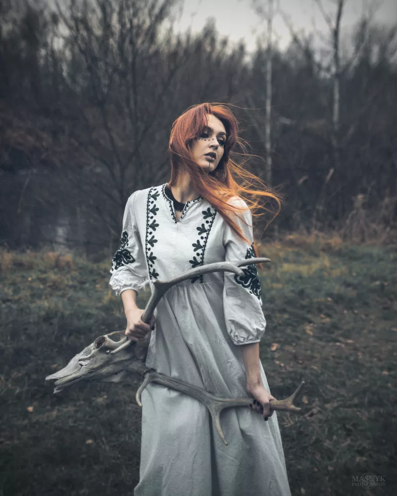 Frau im bestickten Kleid mit Geweih im Wald