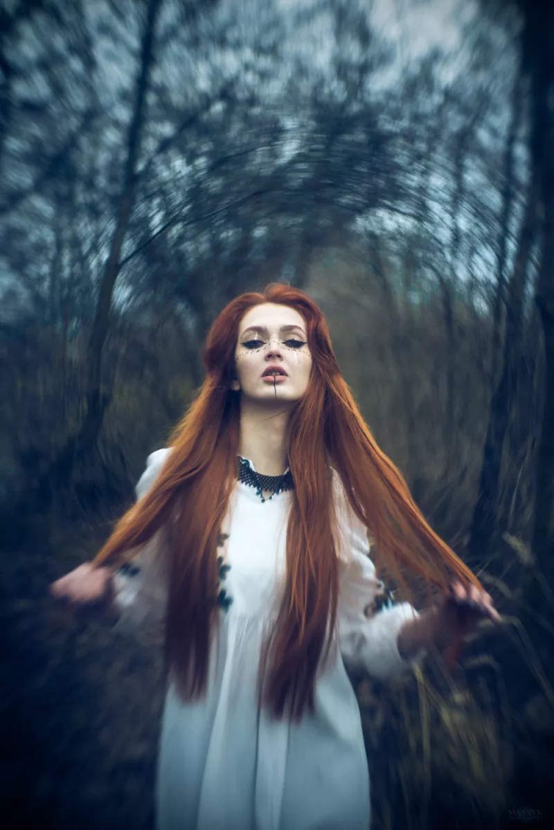 Portrait of a woman in a forest with long red hair and face markings