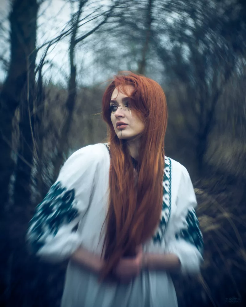 Portrait of a woman in a forest with long red hair and face markings