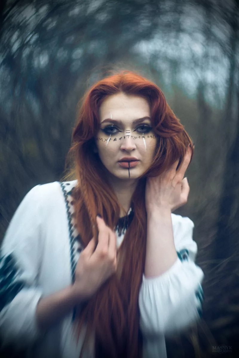 Portrait of a woman in a forest with long red hair and face markings