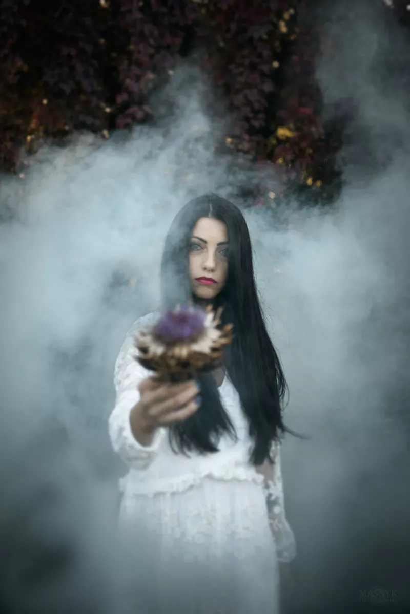 Kobieta w długich włosach i białej sukience stoi we mgle