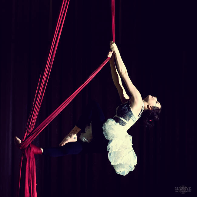 A young woman dances on a hanging fabric.