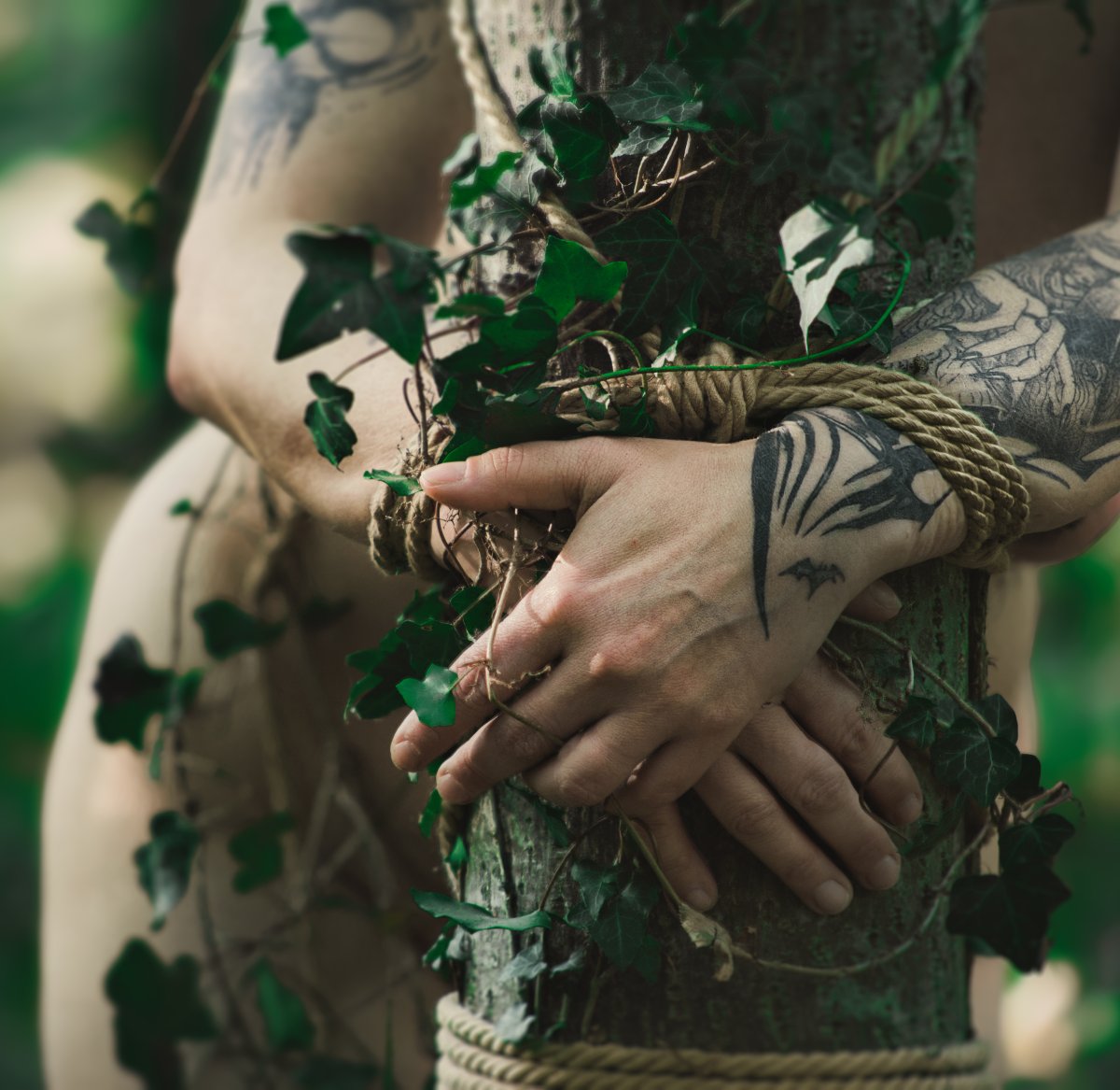 Tattooed hands tied with rope around a tree with ivy