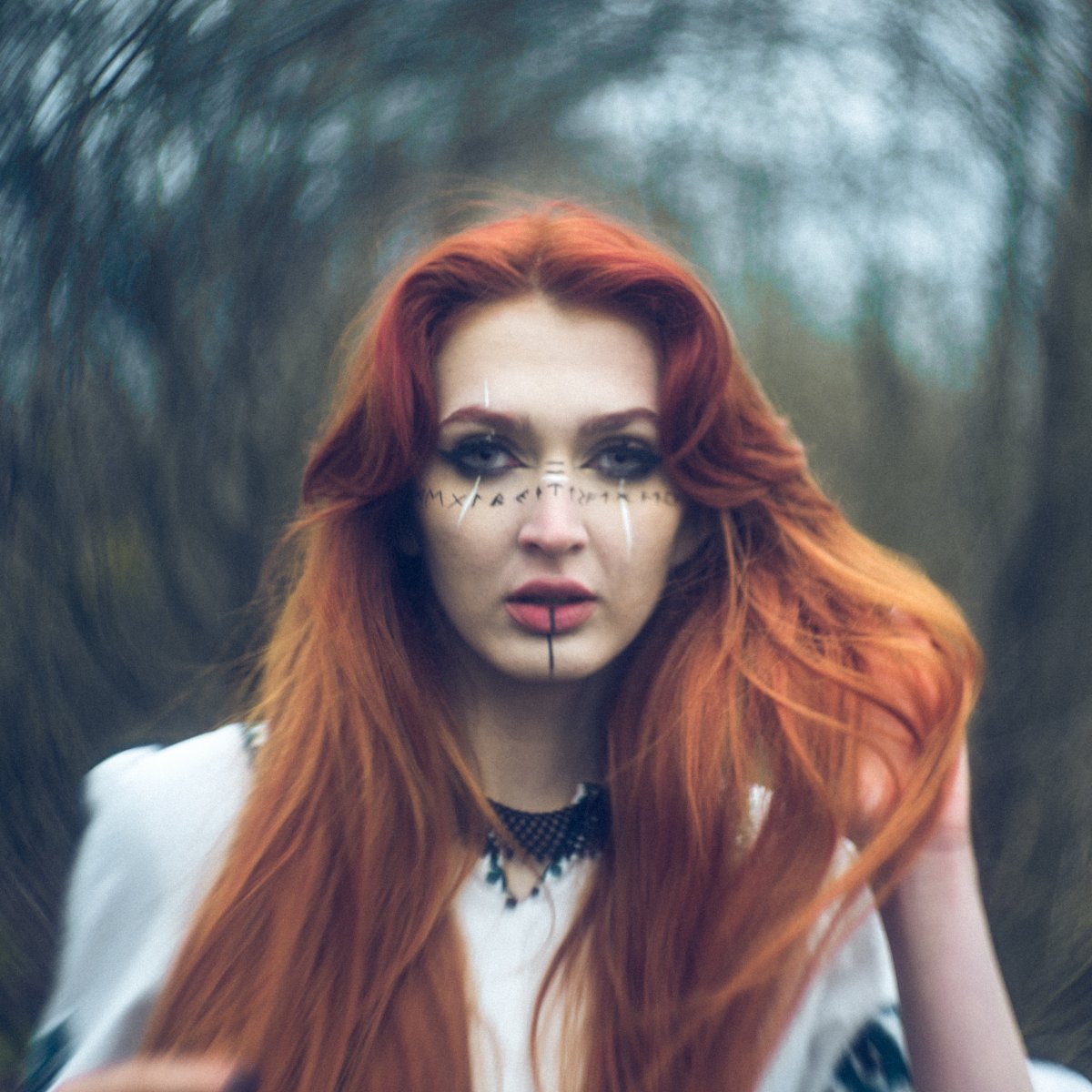 Portrait of a woman in a forest with long red hair and face markings