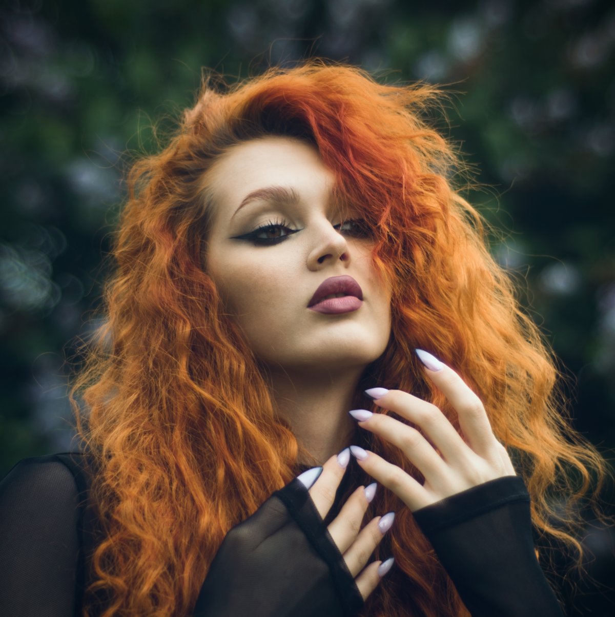 Kobieta z długimi kręconymi rudymi włosami i czarną siateczkową bluzką